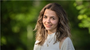 Portrait einer jungen Frau mit braunen Augen und braunem Haar, die im Grünen steht.