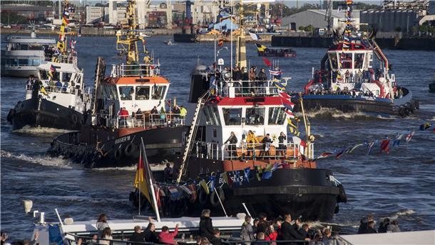 Vier Schlepper werden in einem Hafenbecken von Schaulustigen bejubelt.