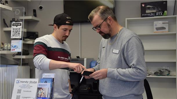 Rainer und Niklas Woge stehen in ihrer Handystube in Nordenham und beraten sich, welches Display das defekte iPhone eines Kunden passen kann. 
