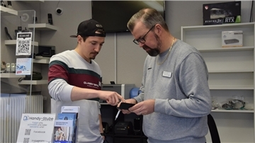 Rainer und Niklas Woge stehen in ihrer Handystube in Nordenham und beraten sich, welches Display das defekte iPhone eines Kunden passen kann. 