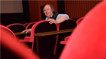 Ein Mann sitzt inmitten von roten Kinostühlen.