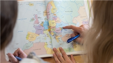 Das Foto zeigt zwei Mädchen wie sie in einem Atlas blättern. 