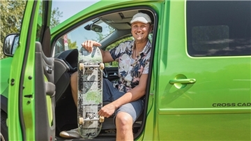 Benjamin Langer sitzt mit einem Skateboard in seinem grünen Cross Caddy.