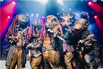 Fünf als Dinosaurier verkleidete Menschen stehen auf einer Bühne. Heavysaurus liefern handgemachten Rock und Metal mit kindgerechten Texten: Die grüngeschuppten Urzeitwesen stehen am 25. April um 17.30 Uhr auf der Bühne in der Stadthalle Bremerhaven. 