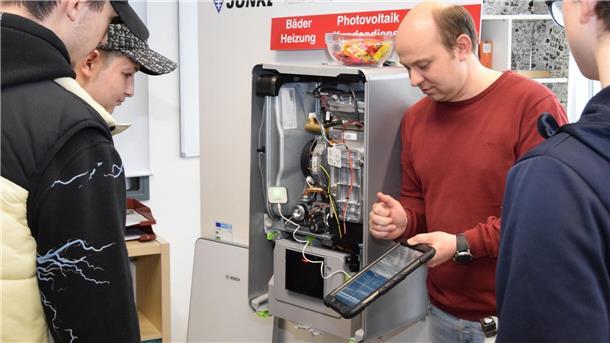 Heizungsbaumeister Alexander Derksen von der Firma Haus & Technik Pape zeigt Neuntklässlern vor einer Therme den Umgang mit einem Diagnosegerät