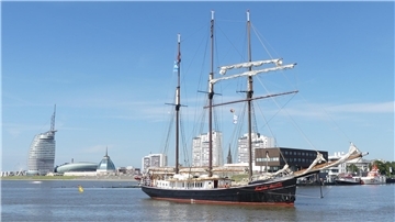 Ein Schiff fährt auf dem Wasser. Im Hintergrund ist die Silhouette einer Stadt zu sehen.