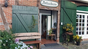 Eingang der Amtsscheune in Bad Bederkesa mit grün gestrichenen Holztoren, Blumenarrangements und einer Bank vor der Tür.