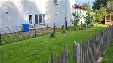 Eine eingezäunte Rasenfläche vor einer weißen Halle. 