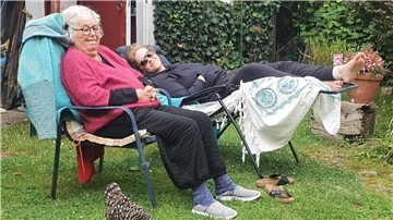 Zwei Frauen in Gartenstühlen davor ein schwarz-weißes Huhn