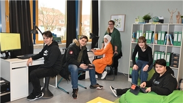 Schüler und eine Lehrerin sitzen in ihrem Redaktionsbüro.