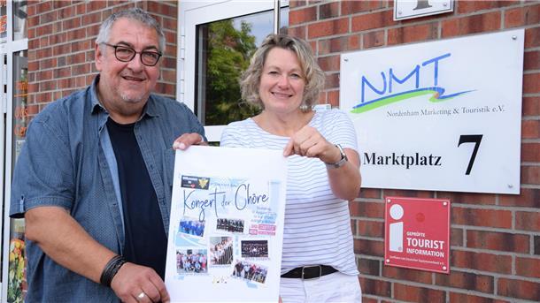 Ein Mann und eine Frau halten ein Plakat des Konzerts der Chöre in den Händen.