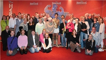 Rund 50 Menschen stehen als Gruppe beisammen. In der Mitte: ein Musicaldarsteller in Hercules-Kostüm.