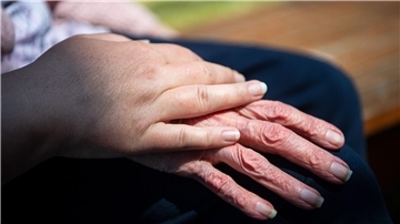 Eine Pflegekraft hält die Hand eines Pflegebedürftigen. 