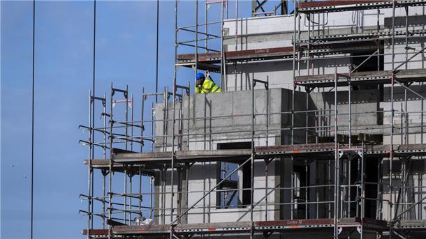 Ein Bauarbeiter steht auf einem Balkon auf einer Baustelle von einem neu gebauten Wohnhaus.