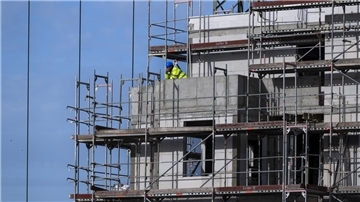 Ein Bauarbeiter steht auf einem Balkon auf einer Baustelle von einem neu gebauten Wohnhaus.