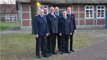 Sechs Feuerwehrleute stehen in festlicher Uniform vor einem norddeutschen Fachwerkhaus.