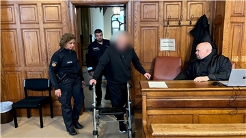 Angeklagter wird am Rollator von Justizbeamten zur Anklagebank geführt. 