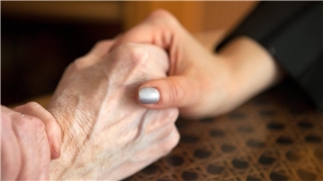Eine Tochter hält die Hand ihrer Mutter im Pflegeheim.