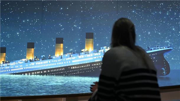 Eine Ausstellungsbesucherin ist von hinten zu sehen. Sie sieht auf einer Leinwand die sinkende "Titanic".