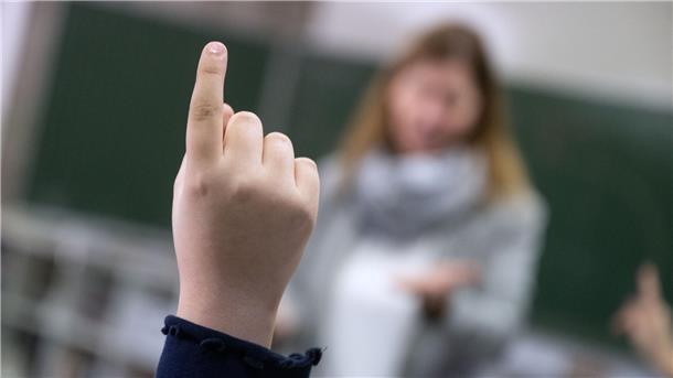 Ein Kind meldet sich im Unterricht. Man sieht nur die Hand. 