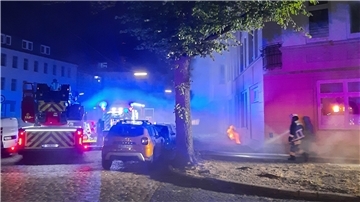Polizei und Feuerwehrwagen stehen nachts auf einer verrauchten Straße.