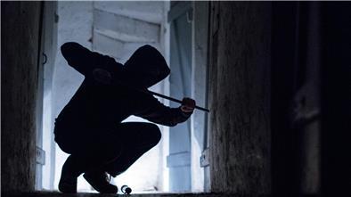 Ein fiktiver Einbrecher hebelt mit einem Brecheisen eine Tür im Keller eines Wohnhauses auf. 