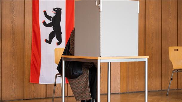 In einem Wahllokal hängt neben einer Wahlkabine eine Berlin-Flagge.