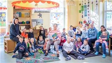 Kindergartenkinder sitzen im Halbkreis neben Vorleseomi Erika