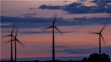 Windräder drehen sich vor Sonnenaufgang und werden von roten Warnleuchten markiert. 