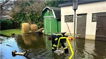 Ein Feuerwehrmann pumpt Wasser aus einem überschwemmten Garten