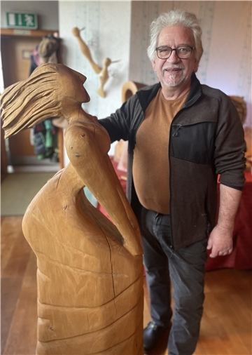 Mann mit Holzfigur. Ein Künstler schnitzt seine Figuren mit einer Kettensäge. 