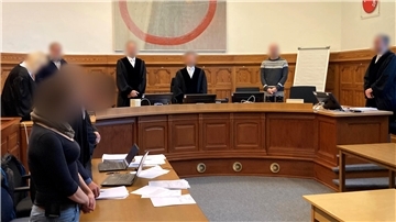 Ein Gerichtssaal zeigt acht Personen, davon eine Frau. Alle Gesichter sind gepixelt.