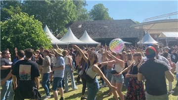 Zahlreiche Menschen tanzen auf einer Wiese.