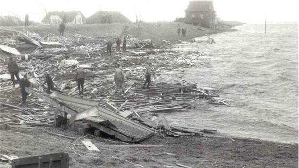 Trümmer einer Strandhalle liegen auf dem Deich. Menschen stehen auf den Trümmern.