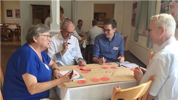 Verschiedene Menschen sitzen an einem Tisch.