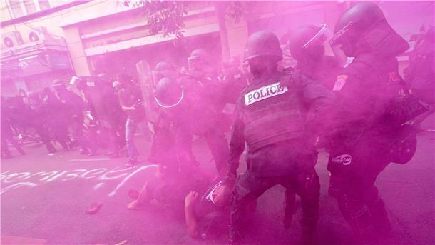 Inmitten einer rosafarbenen Rauchwolke haben Polizisten in Einsatzkleidung einen Demonstranten gepackt.