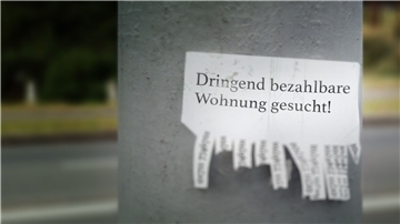 Ein Zettel mit einem Wohnungsgesuch hängt an einem Betonpfeiler.
