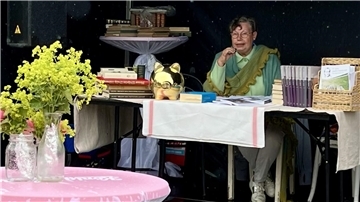 Eine Frau sitzt an einem Tisch und liest etwas vor.