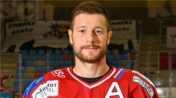 Jan Urbas steht im Trikot in der Eishalle und blickt in die Kamera.