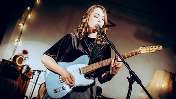 Frau mit Gitarre steht am Mikrofon und singt