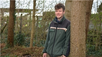 Jasper Robin Krüger lehnt an einem Baum und blickt in die Kamera.