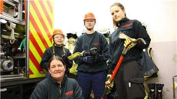 Vier Mitarbeiter der Feuerwehr stehen neben einem Löschfahrzeug.