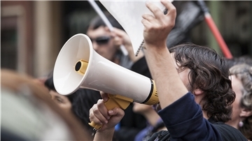 Junger Mann mit Megafon in einer Demonstration.