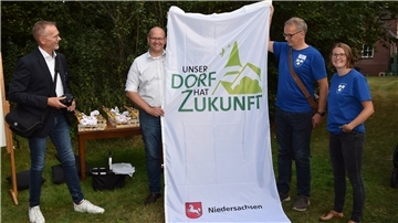 Jury-Leiter Ralf Gebken (von links) vom Landwirtschaftsministerium überreichte bei der Bereisung in Rhade eine Fahne zum Landeswettbewerb „Unser Dorf hat Zukunft“ an Bürgermeister Marco Mohrmann sowie die Ratsmitglieder Olaf Wendelken und Raphaela Vink, die durch die Präsentation führten.  