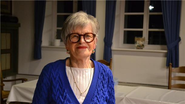 Eine ältere Frau im leuchtend blauen Strickpullover lächelt in die Kamera.