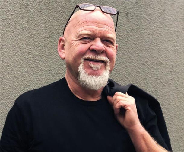 Ein Mann in schwarzer Kleidung hat einen grauen Bart und lächelt. Eine Brille ist auf seiner Glatze. Er lächelt. Kabarettist Bernd Gieseking nimmt das Publikum mit auf seine witzige Reise durchs Älterwerden – und zur Zugspitze.