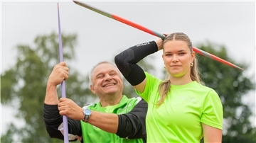 Ein Trainer hält einen Speer, während sein Schützling einen Speer über den Kopf hält.