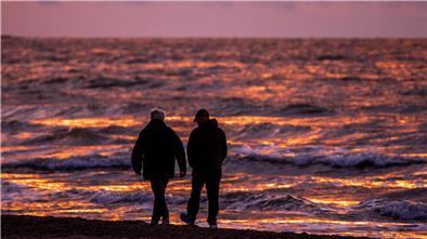 Spaziergänger sind nach Sonnenuntergang am Strand von Warnemünde an der Ostsee unterwegs.