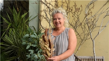 Eine Frau hält einen trockenen Strauß vor ihrem Blumenladen in den Händen. 