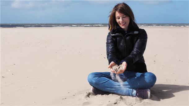 Frau sitzt im Sand am Strand und hält Sand in den Händen